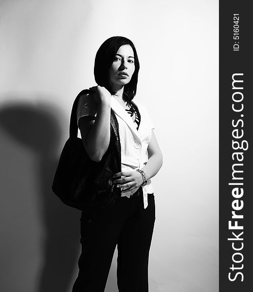 A black and white high-key portrait about a pretty trendy lady with black hair who is looking ahead and she has an attractive look. She is wearing black pants, a white coat and a stylish handbag. A black and white high-key portrait about a pretty trendy lady with black hair who is looking ahead and she has an attractive look. She is wearing black pants, a white coat and a stylish handbag.