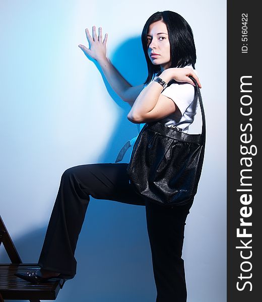 A high-key portrait about a cute trendy lady with black hair who is leaning against the wall, she is lifting up her leg and she has an attractive look. She is wearing black pants, a white coat and a stylish handbag. A high-key portrait about a cute trendy lady with black hair who is leaning against the wall, she is lifting up her leg and she has an attractive look. She is wearing black pants, a white coat and a stylish handbag.