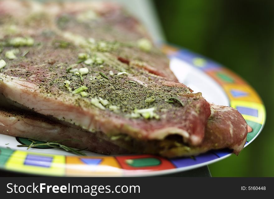 Raw marinated porterhouse steak on a plate. Pepper, rosemary and garlic seasoning is visible. Raw marinated porterhouse steak on a plate. Pepper, rosemary and garlic seasoning is visible.