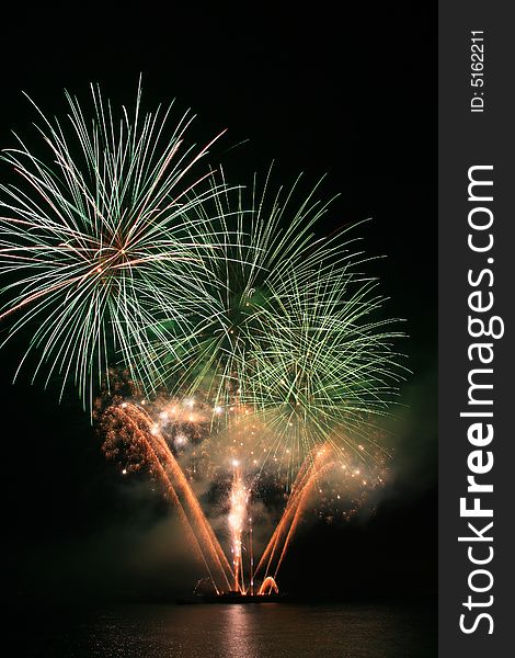 Bright green and orange fireworks against the dark sky