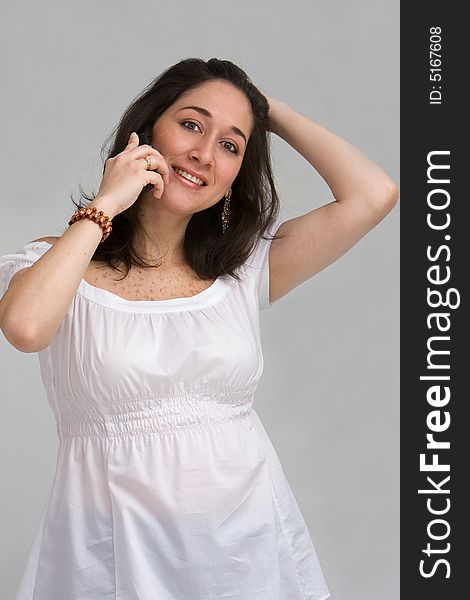 A beautiful latina lady dressed in white having a happy conversation on a cell phone, isolated on gray. A beautiful latina lady dressed in white having a happy conversation on a cell phone, isolated on gray