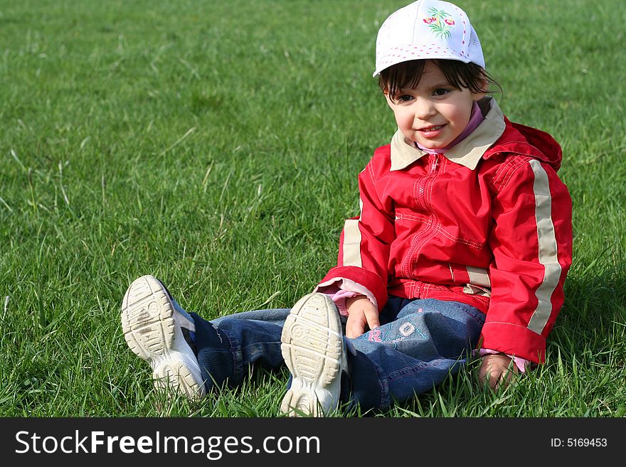 Little girl in the park sitting on green grass