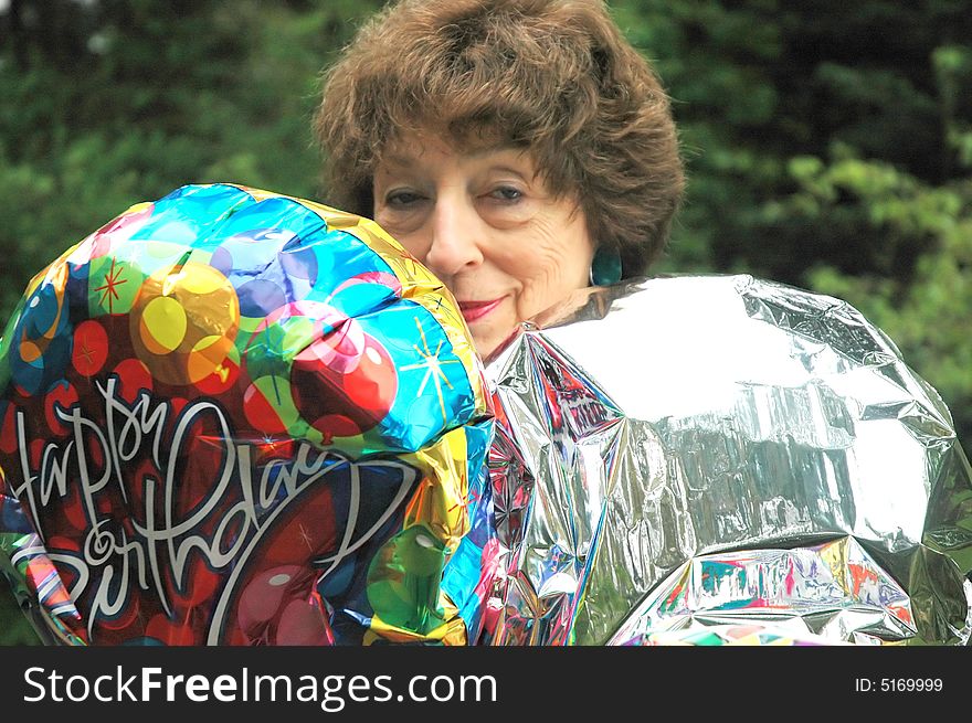 Mature female senior relaxing at home on her outdoor deck with happy birthday balloons.