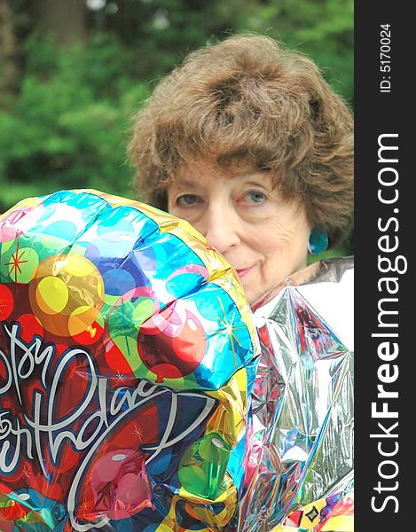 Mature female senior relaxing at home on her outdoor deck with happy birthday balloons.