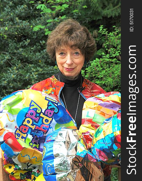 Mature female senior relaxing at home on her outdoor deck with happy birthday balloons.