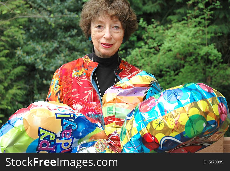 Mature female senior relaxing at home on her outdoor deck with happy birthday balloons.