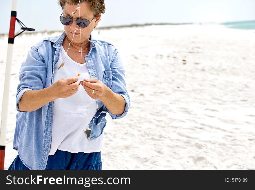 Mature woman baiting her fishing hooks at the beach; she's catching pompano!. Mature woman baiting her fishing hooks at the beach; she's catching pompano!