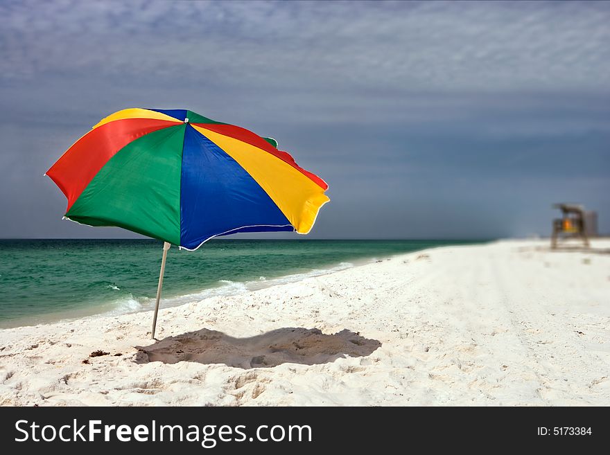 Colorful beach umbrella on a deserted beach as a storm approaches on the dark horizon. Colorful beach umbrella on a deserted beach as a storm approaches on the dark horizon