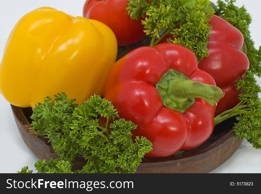 Red and yellow pepper with greens in a basket on a white background. Red and yellow pepper with greens in a basket on a white background.