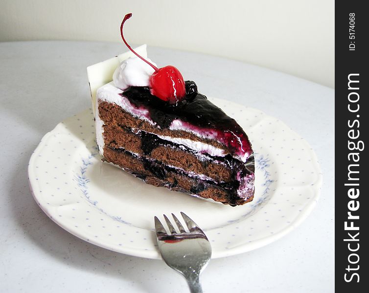 A slide of black forest cake with cherry on top and white chocolate