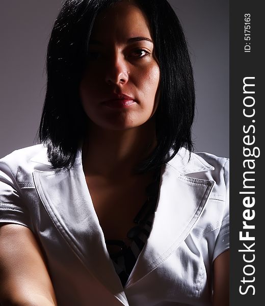 A low-key portrait about an attractive trendy girl with black hair who is looking ahead and she has a glamorous look. She is wearing a white stylish coat. A low-key portrait about an attractive trendy girl with black hair who is looking ahead and she has a glamorous look. She is wearing a white stylish coat.