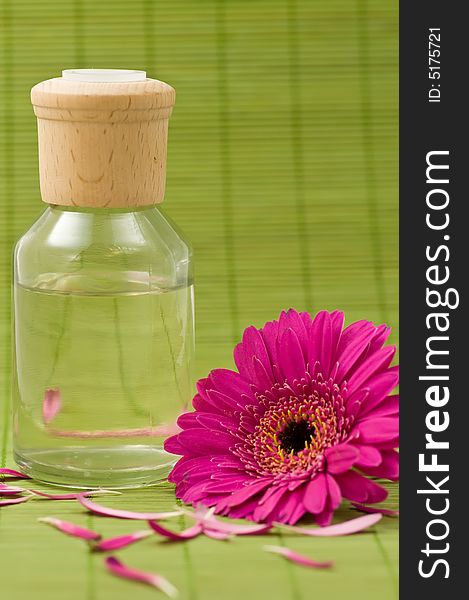 Aromatherapy bottle, pink flower and petals on green bamboo, focus on bottle