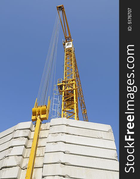 Tall yellow construction-crane with large counter-weights set against blue sky. Tall yellow construction-crane with large counter-weights set against blue sky