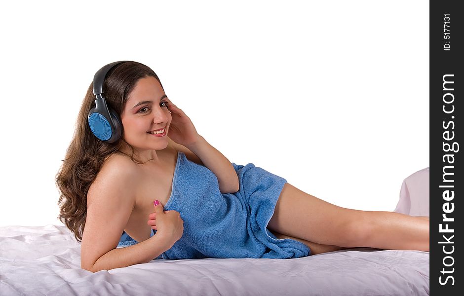 A beautiful girl, lying wrapped in a blue towel, wearing headphones, enjoying the music. A beautiful girl, lying wrapped in a blue towel, wearing headphones, enjoying the music