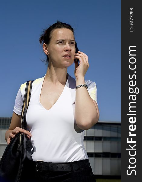 A woman calling on a cell phone in front of commercial buildings with blue sky. A woman calling on a cell phone in front of commercial buildings with blue sky