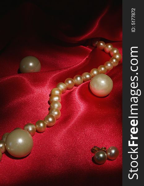 Pearl earrings and necklace on red silk background