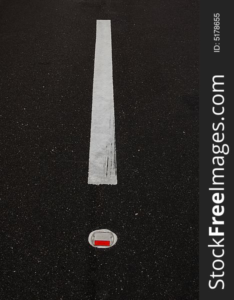 A road line with a red reflector, it looks like an exclamation point.  Great for highway and driving material.