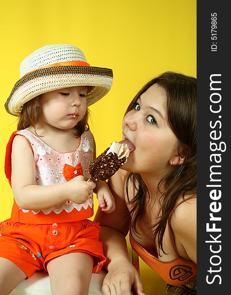 Two pretty sisters are eating ice-cream on yellow background. Two pretty sisters are eating ice-cream on yellow background