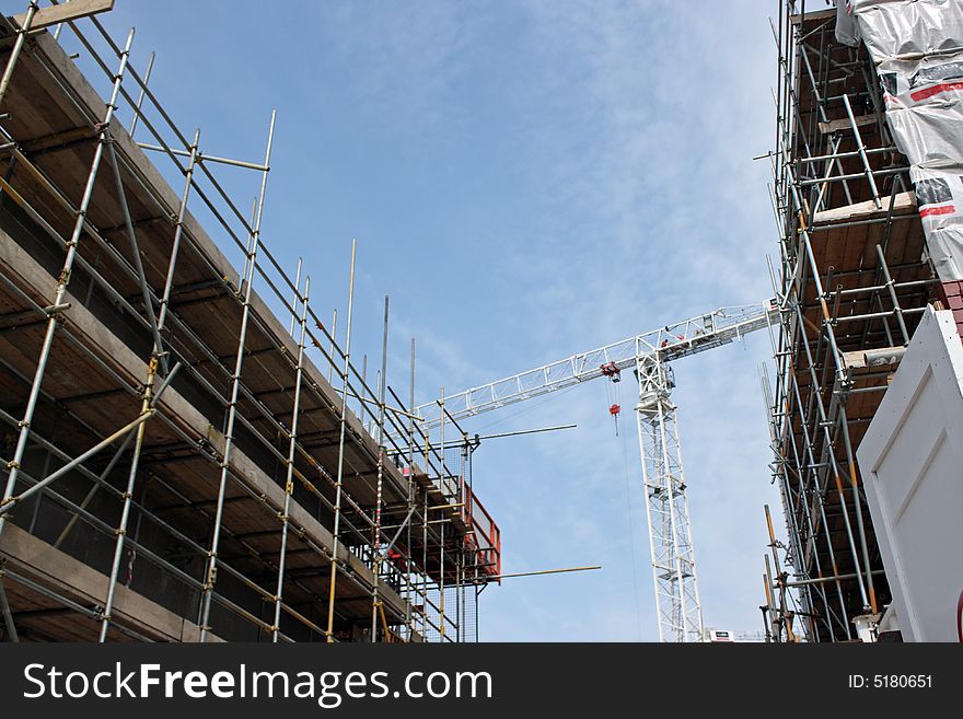 Construction crane against a blue sky with scaffold covered buildings both side. Construction crane against a blue sky with scaffold covered buildings both side