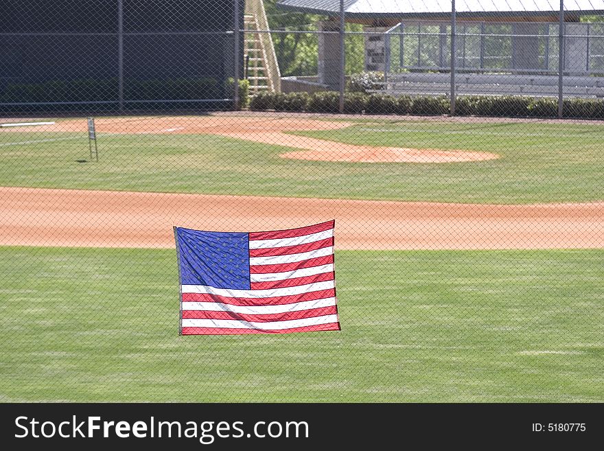 A view of a softball or baseball field from beyond the outfield fence with an American Flag. A view of a softball or baseball field from beyond the outfield fence with an American Flag