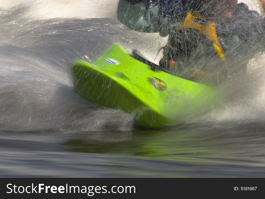 A close-up of a whitewater kayaker in a wave with spray. A close-up of a whitewater kayaker in a wave with spray