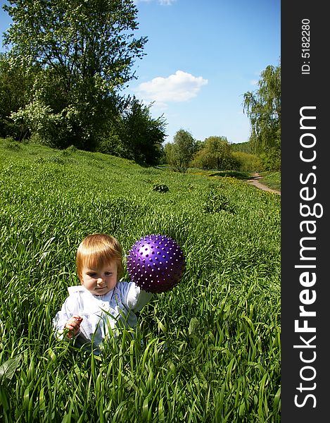 The beautiful girl sits on a grass with a ball