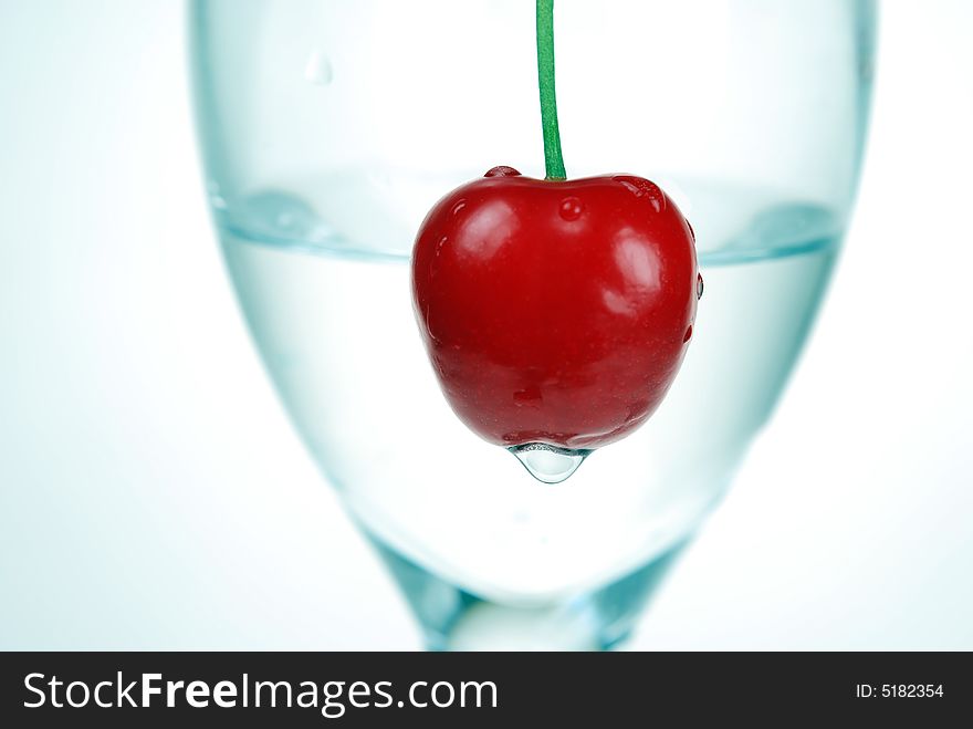 Close up to Sour cherry with water drop in front of a glass filled with tonic water