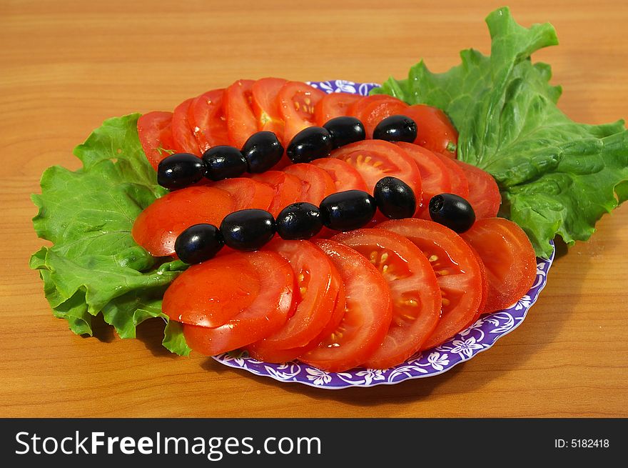 Tomatoes, leaves of salad and olives on a round plate. Tomatoes, leaves of salad and olives on a round plate