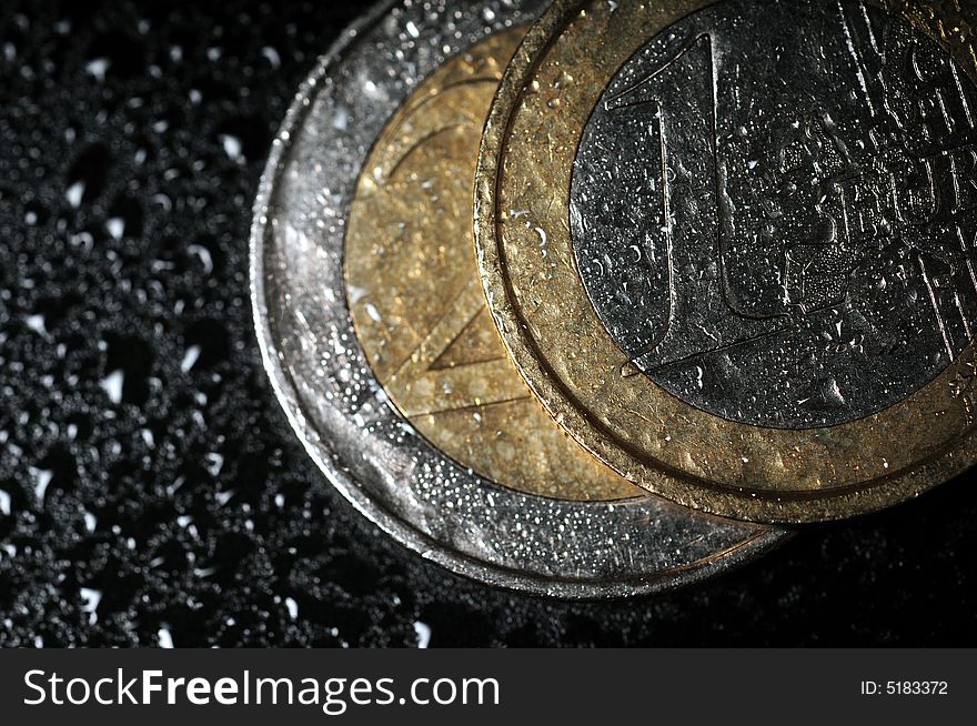 A close up with euro coins over a wet black background