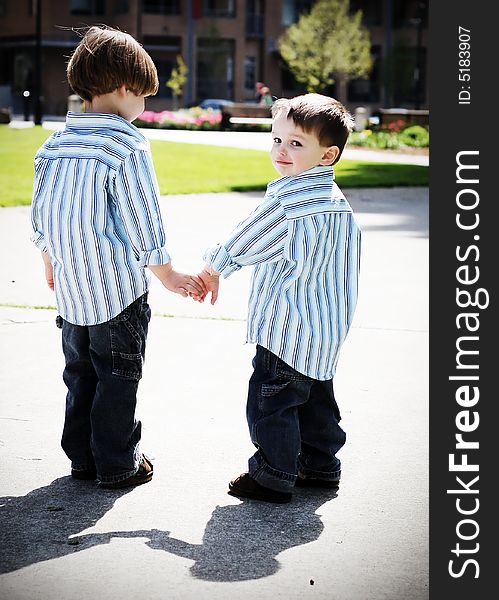 Two identically dressed brothers holding hands in a park. High-contrast style