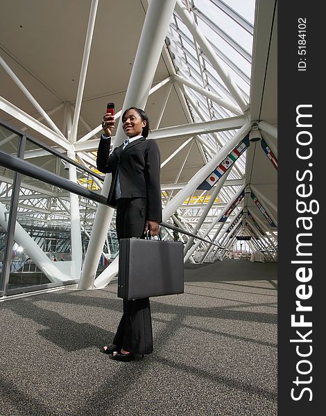 Businesswoman standing in an office atrium smiling as she takes a picture on her cellphone. Lobby has international flags adorning it. Vertically framed shot. Businesswoman standing in an office atrium smiling as she takes a picture on her cellphone. Lobby has international flags adorning it. Vertically framed shot.