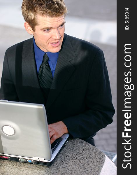 Businessman sitting down at table typing on laptop looking away. Businessman sitting down at table typing on laptop looking away