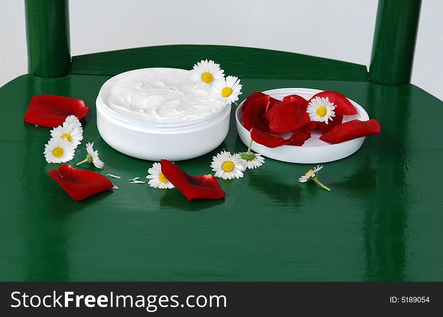 White creme with rose and daisy petals over green. White creme with rose and daisy petals over green