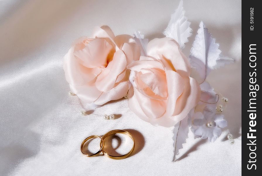 Wedding rings with artificial roses on white silk.