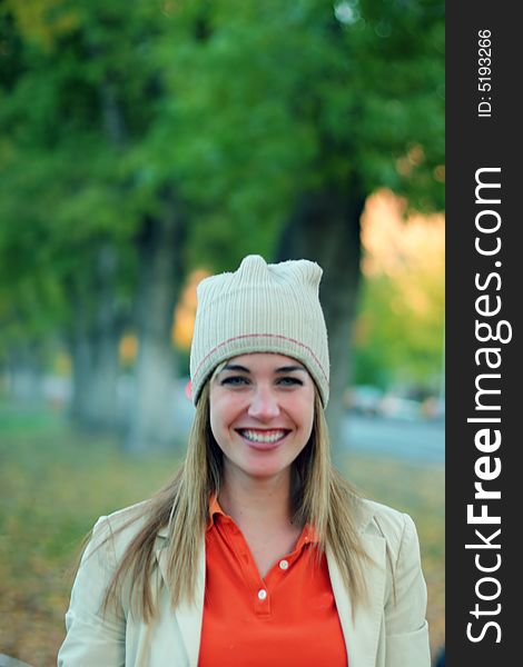 Young woman smiling outside in the fall with a cap and jacket on while wearing an orange shirt outside in a park. Young woman smiling outside in the fall with a cap and jacket on while wearing an orange shirt outside in a park