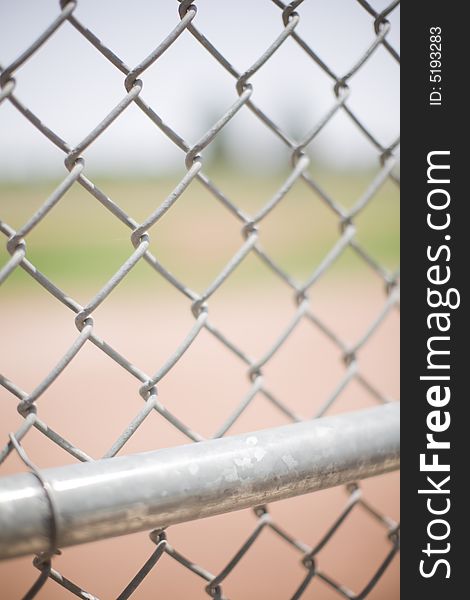 Close-up of a baseball fence outside in the summer with a chain link fence in the front and a baseball field in the background. Close-up of a baseball fence outside in the summer with a chain link fence in the front and a baseball field in the background