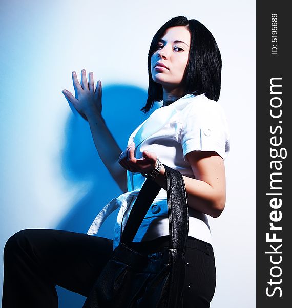 A high-key portrait about a cute trendy lady with black hair who is leaning against the wall, she is lifting up her leg and she has a glamorous look. She is wearing black pants, a white coat and a stylish handbag. A high-key portrait about a cute trendy lady with black hair who is leaning against the wall, she is lifting up her leg and she has a glamorous look. She is wearing black pants, a white coat and a stylish handbag.