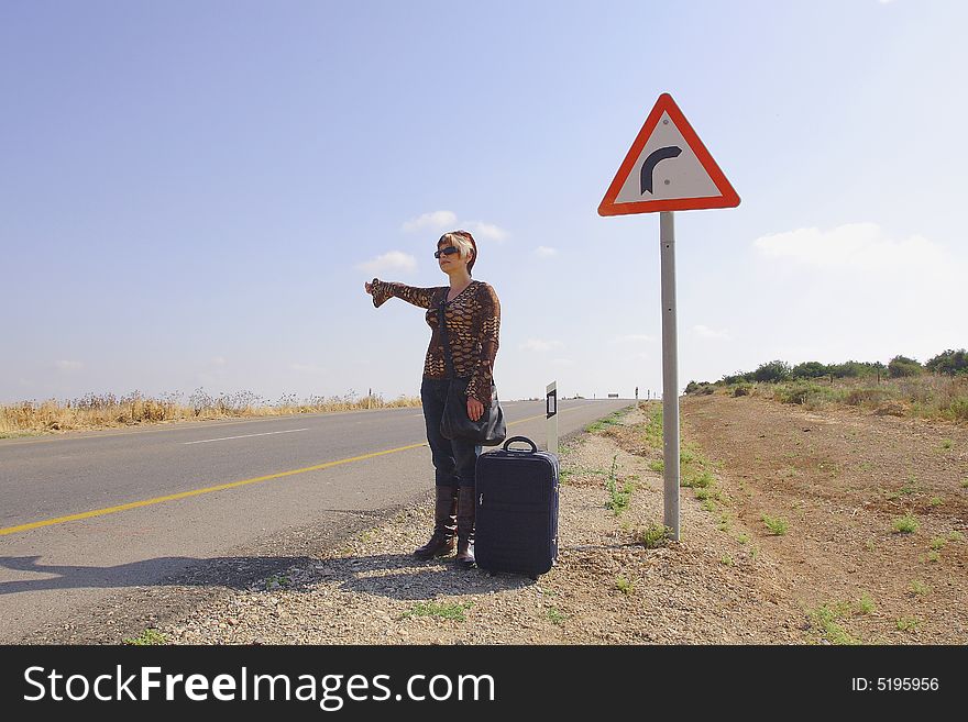 A young female hitch-hiker with her luggage. A young female hitch-hiker with her luggage