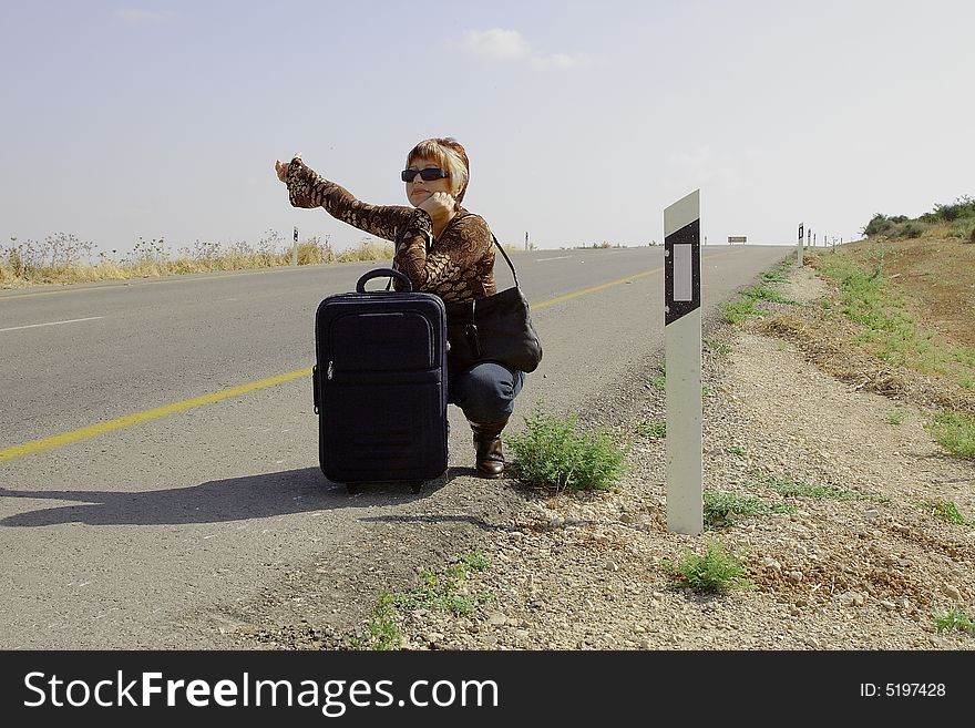 A young female hitch-hiker with her luggage. A young female hitch-hiker with her luggage