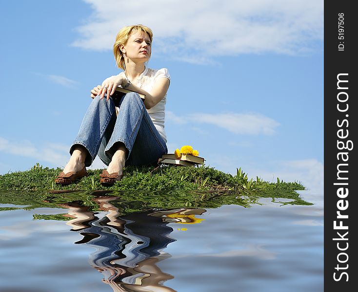 Female student outdoor on green grass with books and blue sky on background and reflection