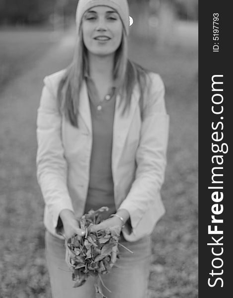 Young woman holding a bunch of leaves outside in the winter time wearing a cap and jacket with a smile on her face. Young woman holding a bunch of leaves outside in the winter time wearing a cap and jacket with a smile on her face