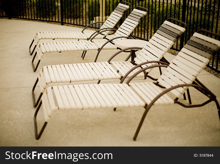 A group of four pool chairs next to each other outside during the summer time