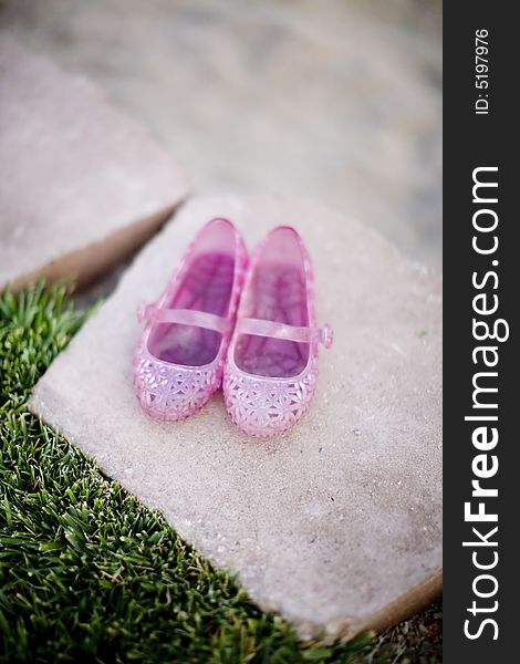 Little girl shoes that are pink sitting together on a brick wall next to grass outside in the spring