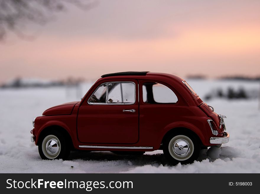 Red retro toy car in the snow with sunset landscape as background. Red retro toy car in the snow with sunset landscape as background