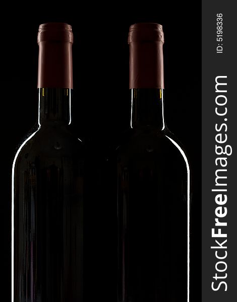Two red wine bottles on a black background with rim light. Two red wine bottles on a black background with rim light