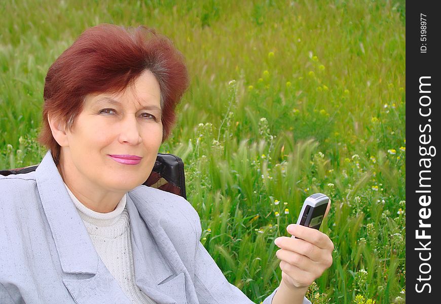 Mature woman rests on nature with a mobile telephone. Mature woman rests on nature with a mobile telephone.