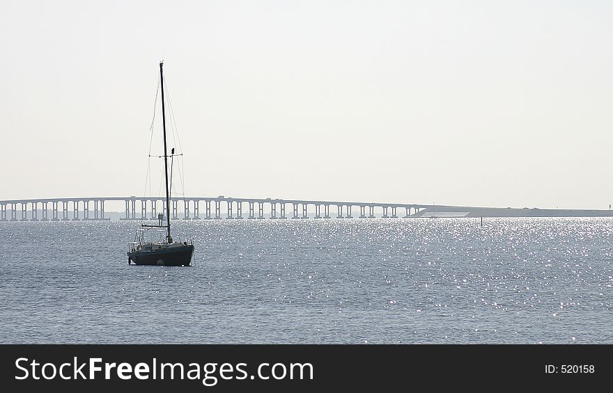 Sailboat at anchor in the Indian River, Rockledge, Florida. There's lots of sky and water and there's a bridge in the distance Photo ID: BeachScenes00001