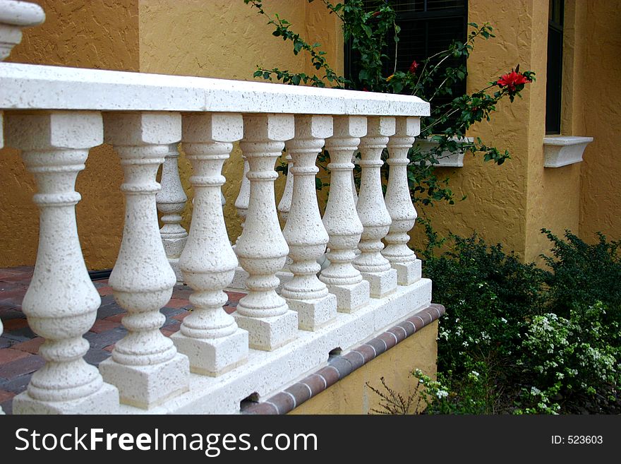 White columns and railing at entrance of home, with red flower peaking out. White columns and railing at entrance of home, with red flower peaking out