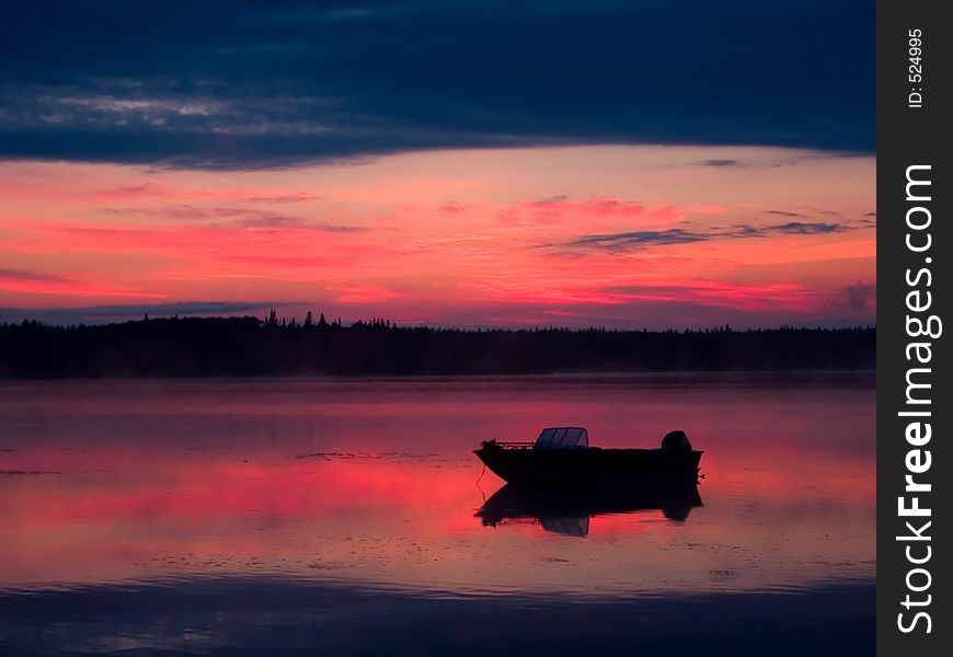 A boat stands moored in shallow water before sunrise.