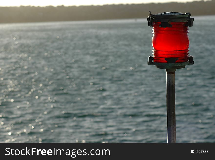 A red warning beacon in the late afternoon sun near the ocean sea-wall.